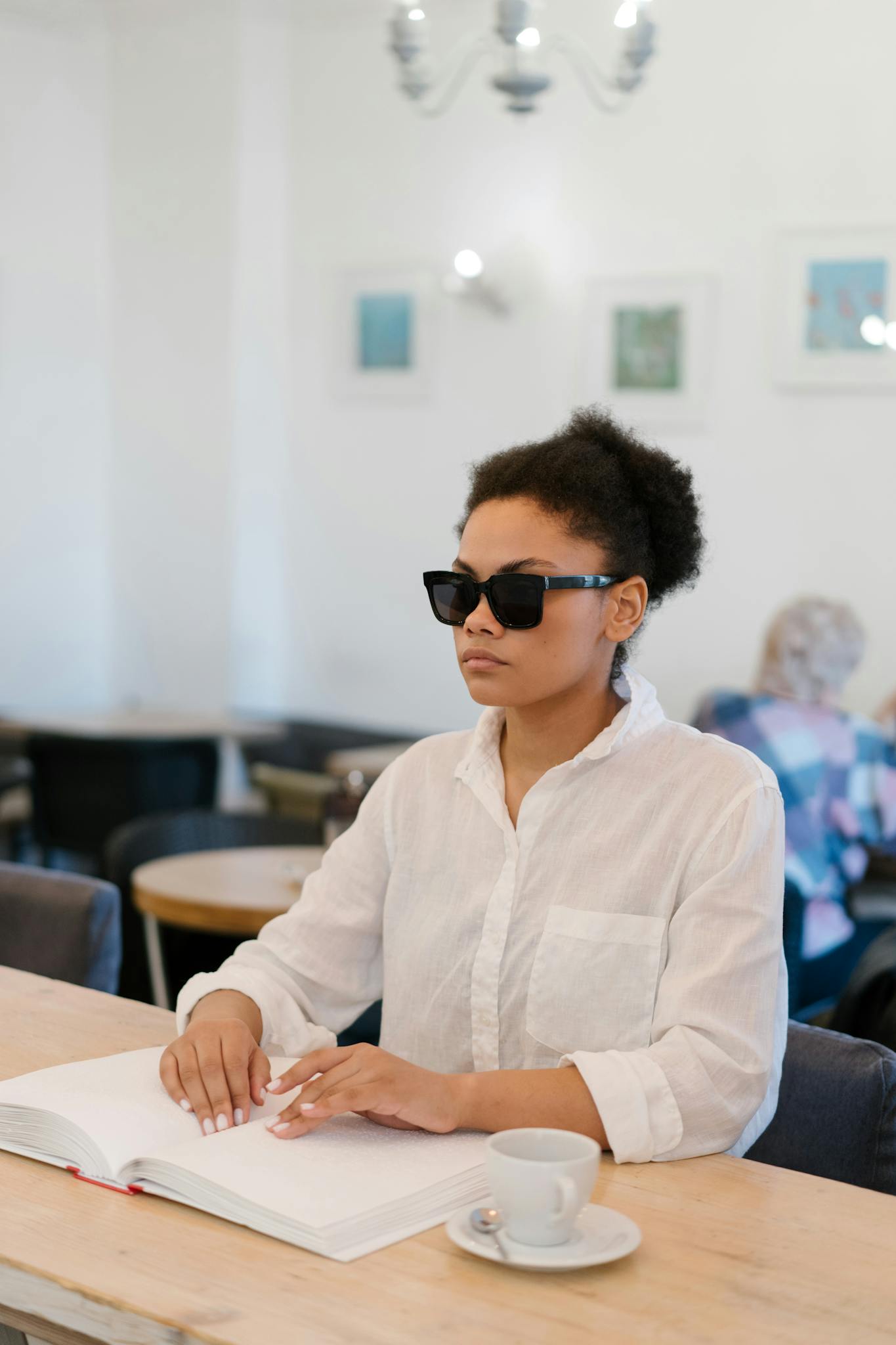 An African American woman with visual impairment reads Braille in a cafe setting.